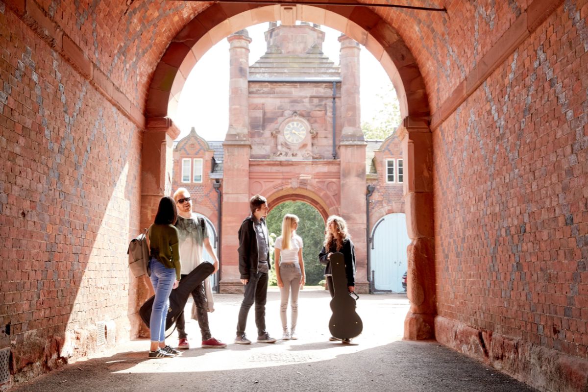 Students standing under an archway, carrying musical instruments