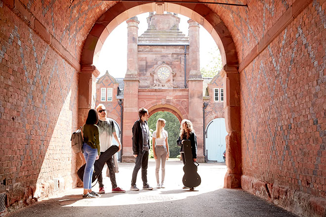Students standing under an archway, carrying musical instruments